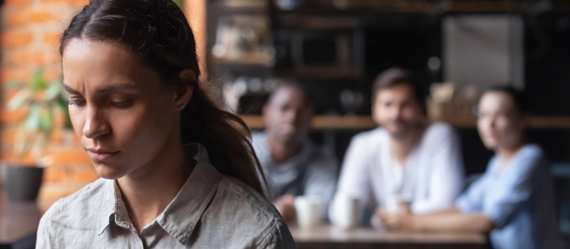 Upset mixed race woman suffering from bullying, sitting alone in cafe